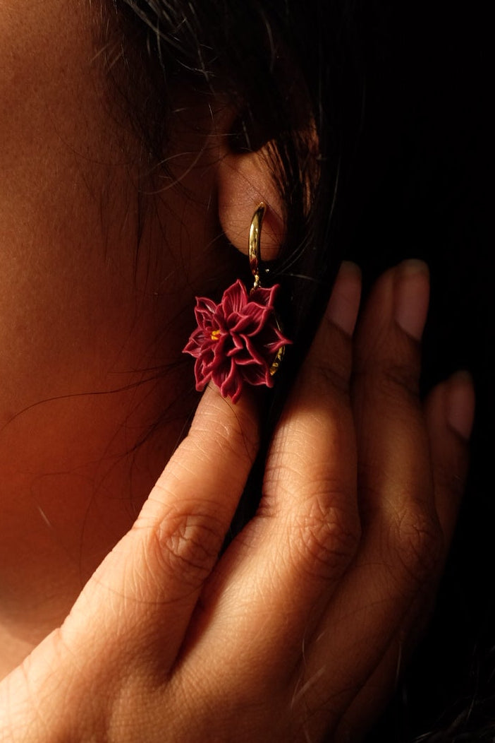 Close-up of a hand adjusting a floral earring on a dark background